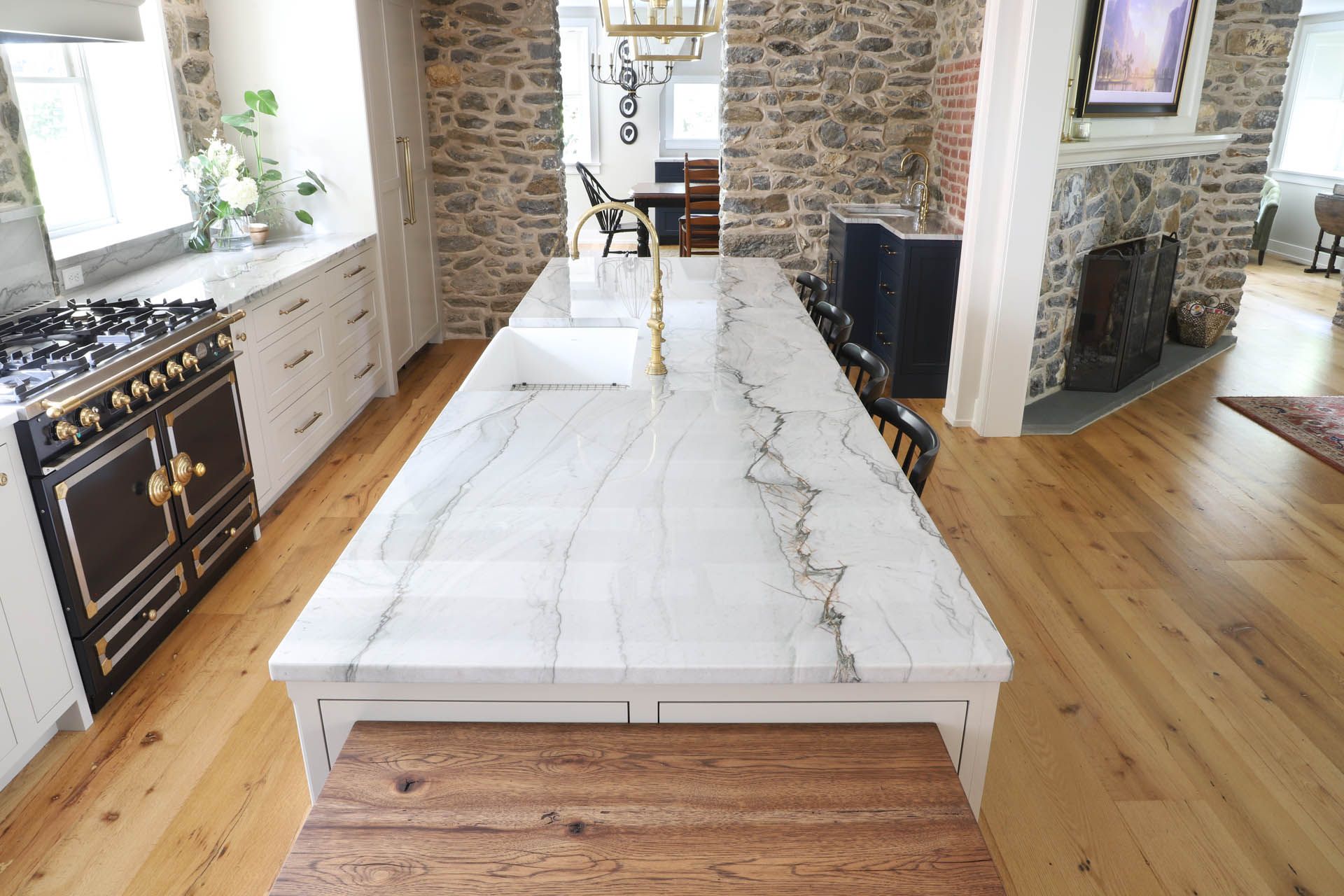 Kitchen with white island, marble countertop, wooden floor, and a stone wall.