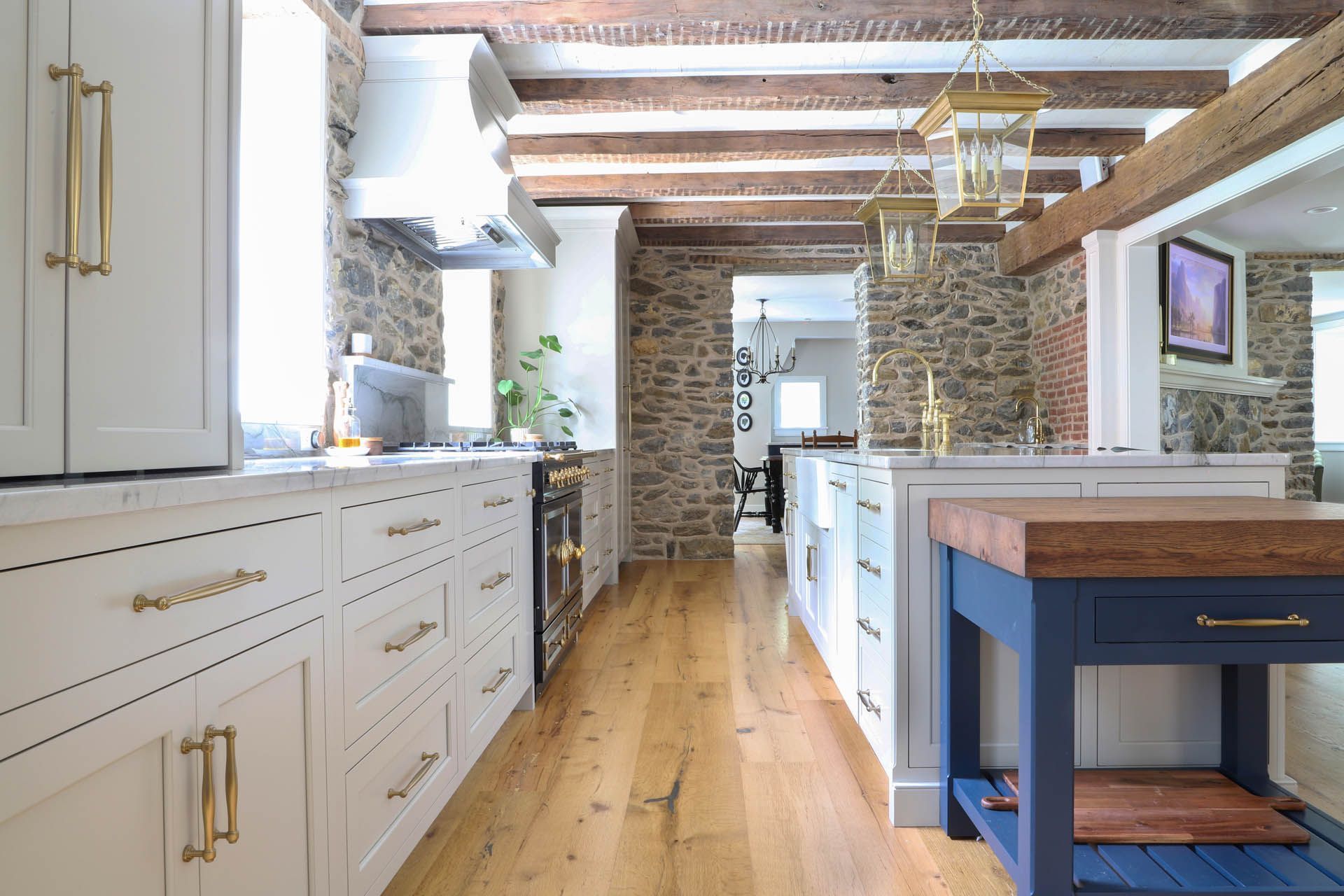 Elegant kitchen with stone walls, wooden beams, white cabinets, and a blue island.