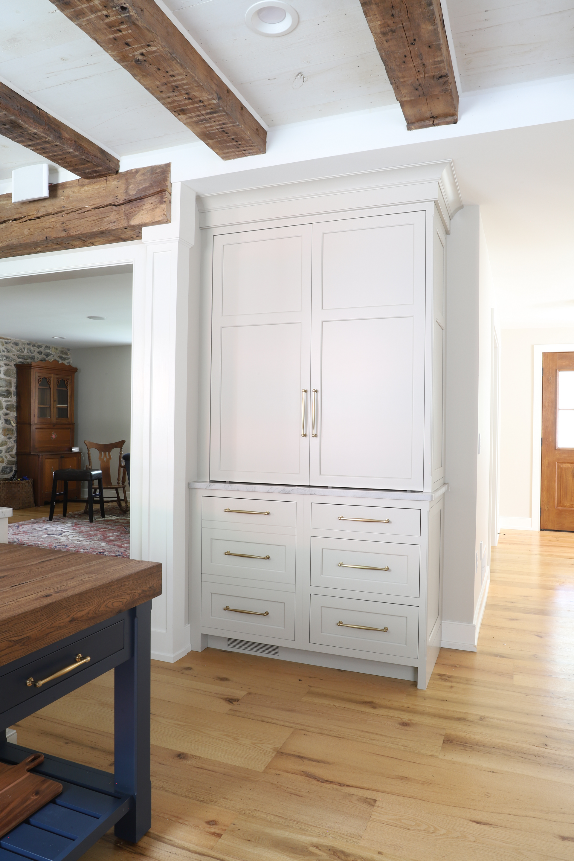 White kitchen pantry with drawers and cabinets, wood floors, and exposed ceiling beams.