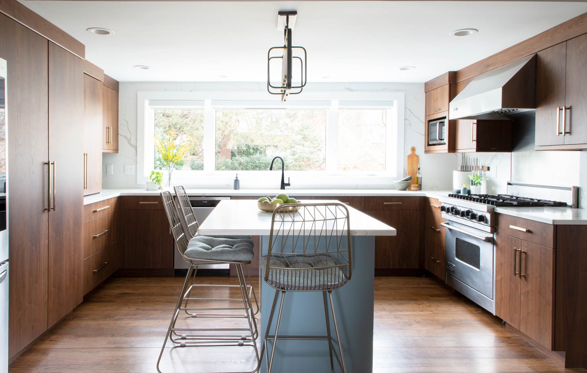 A U-shaped kitchen with brown wood cabinets, white countertops, stainless steel appliances, and a central blue island.