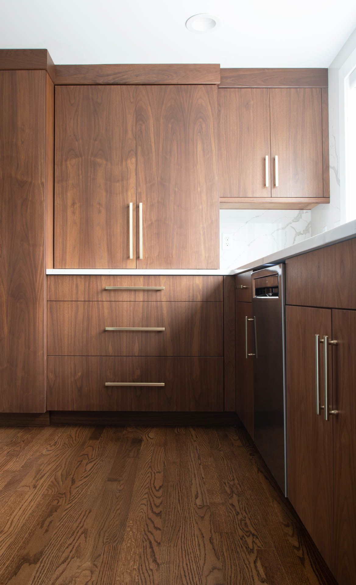 Modern kitchen with dark wood grain cabinetry, stainless steel dishwasher, and hardwood flooring.