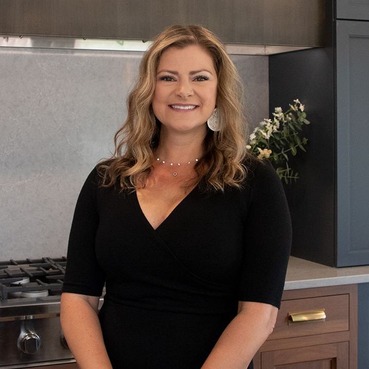 A woman in a black dress is smiling in a kitchen