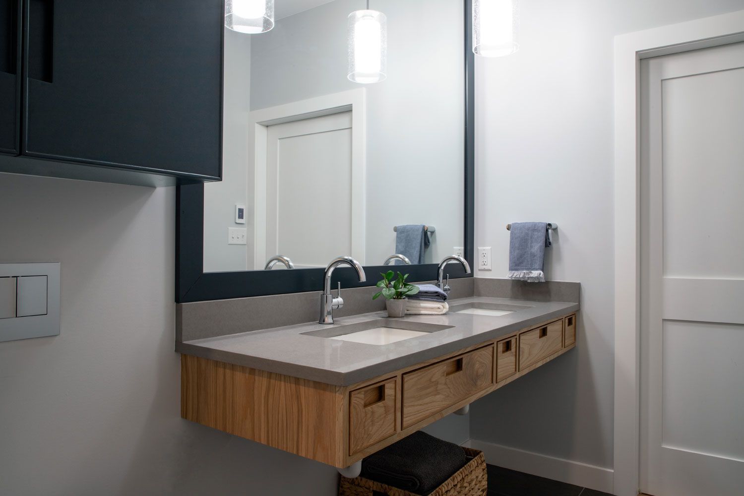 Modern bathroom vanity with light wood drawers, gray countertop, double faucets, large mirror, and black wall cabinet.