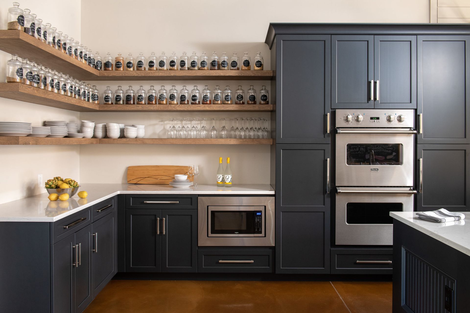 Modern kitchen with blue cabinets, stainless steel appliances, and wooden shelves displaying jars and glassware.