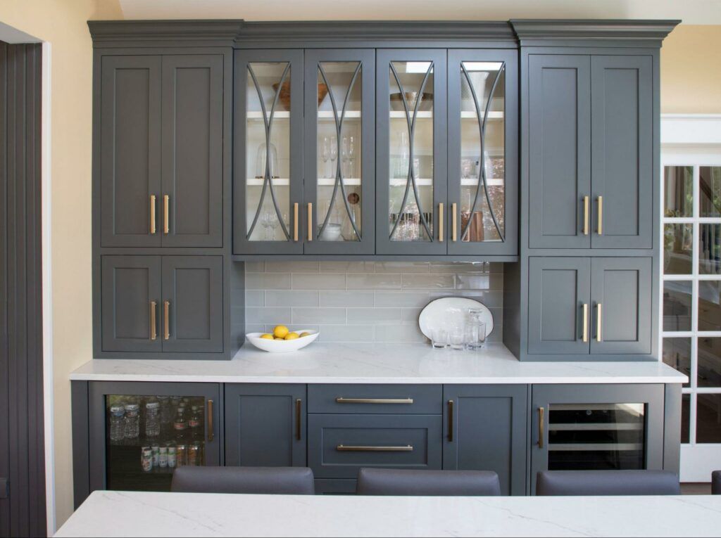 Charcoal gray built-in cabinetry with glass-front uppers, brass hardware, and built-in wine storage flanking a counter.