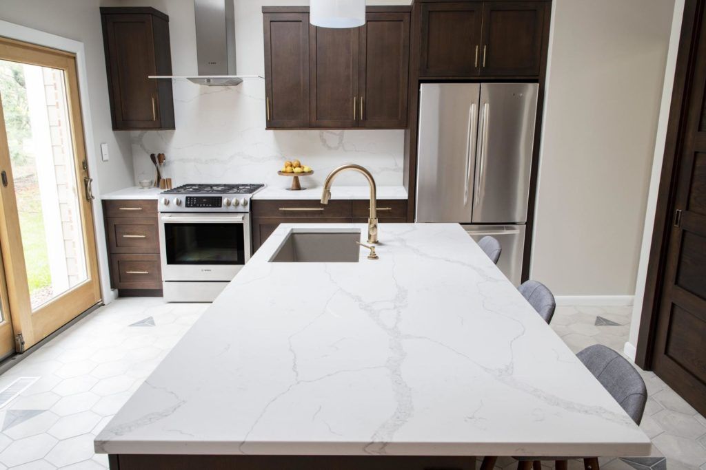 Modern kitchen with white countertops, dark cabinets, stainless steel appliances.