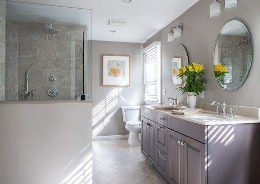 Spacious bathroom with gray walls, glass shower, double vanity, and sunny window.
