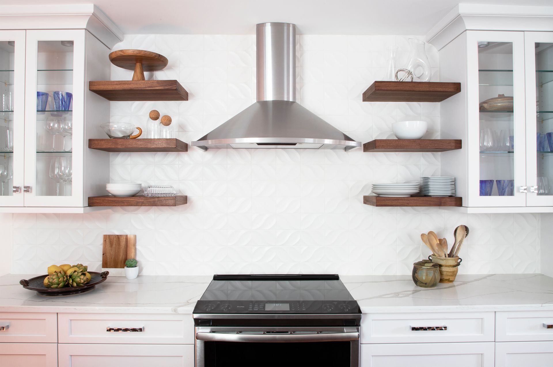 A kitchen with a stove , oven , shelves and a hood.