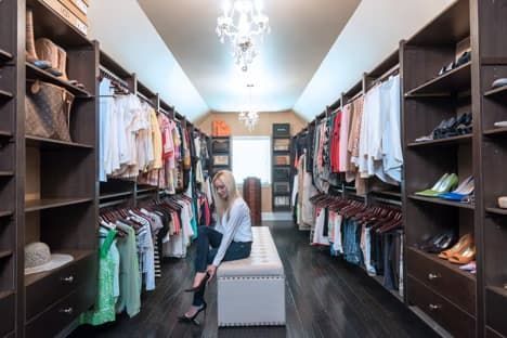 Walk-in closet with clothing on shelves and a person sitting on a bench in the center