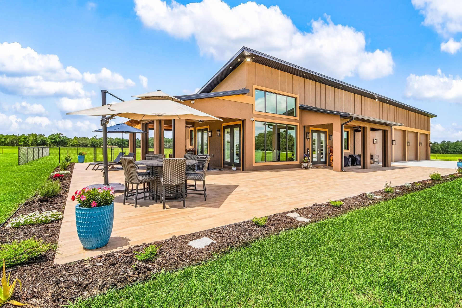 Modern house with brown siding, large patio, outdoor dining set, blue sky.