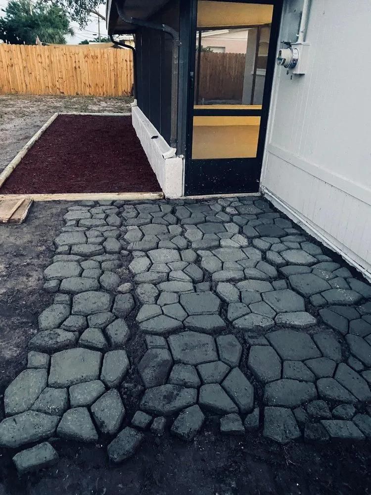 Stone-paved patio beside a house with a dark-framed door and fenced yard