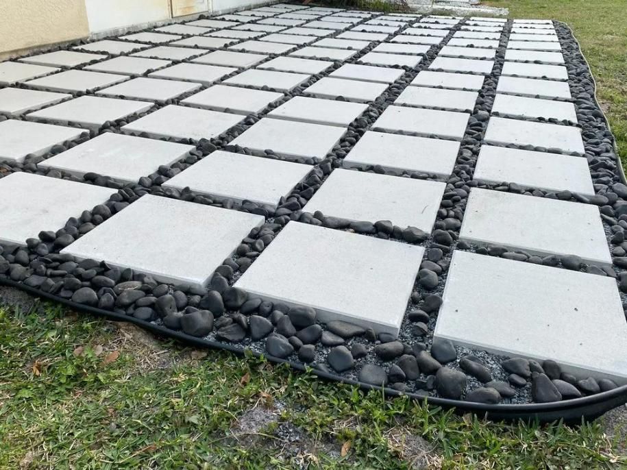 Raised concrete pavers in a grid with dark stone borders on a grassy yard