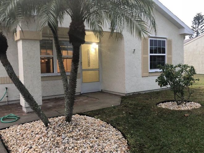 Front entrance of a house with a yellow door, palm trees, and decorative white rock landscaping.