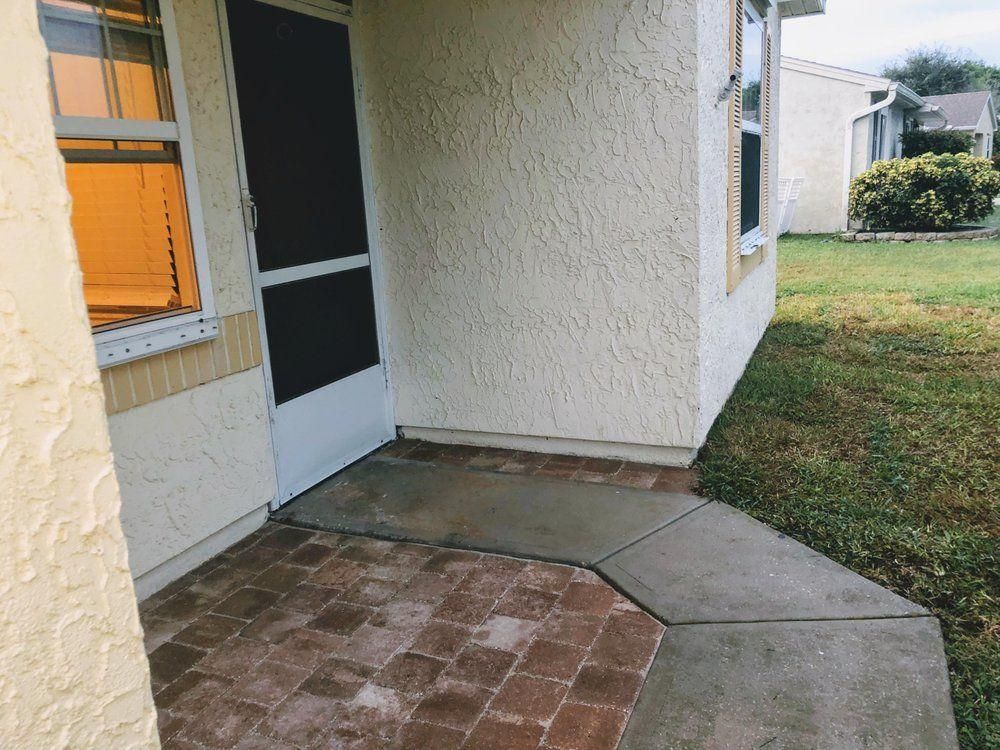 Brick patio and concrete walkway beside a house entrance with a white screen door.