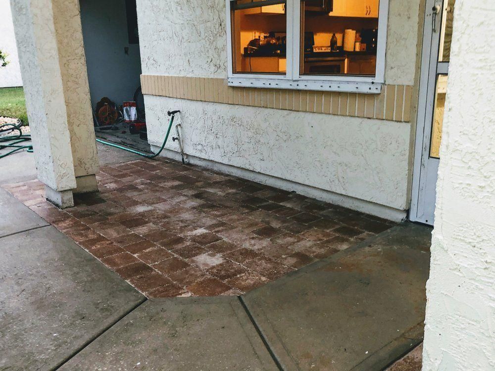 Covered patio with wet brick and concrete flooring beside a stucco house window