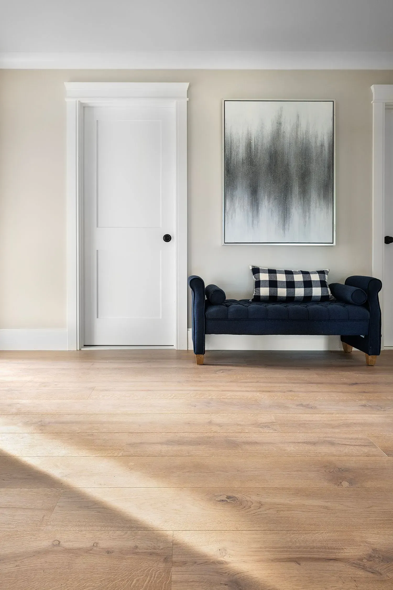 A hallway with light-colored cork flooring, a navy blue bench with a black and white pillow, and abstract art.