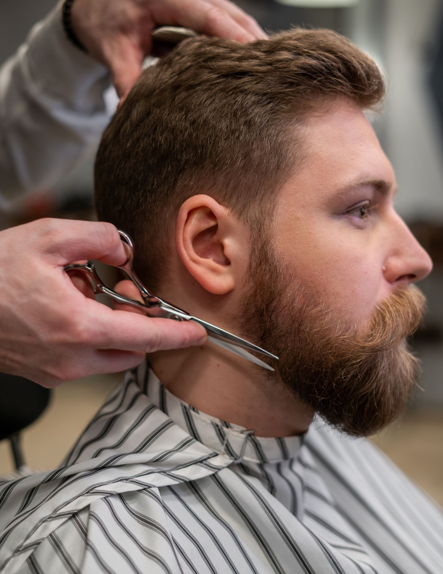 A man with a beard is getting his hair cut by a barber.