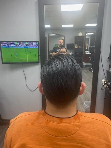 A man is sitting in front of a television in a barber shop.