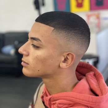 A young man wearing a red hoodie is getting his hair cut by a barber.