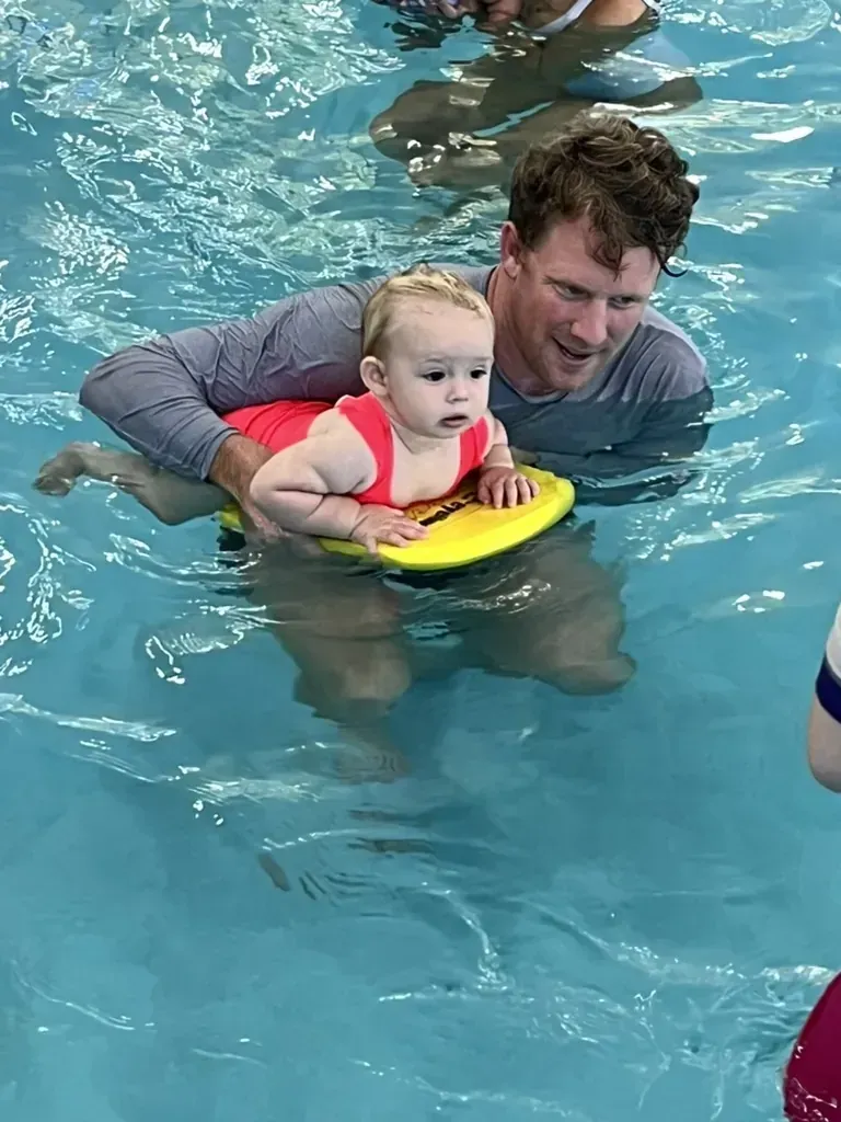 A dad supporting his baby on a kickboard during a Pod Squad lesson