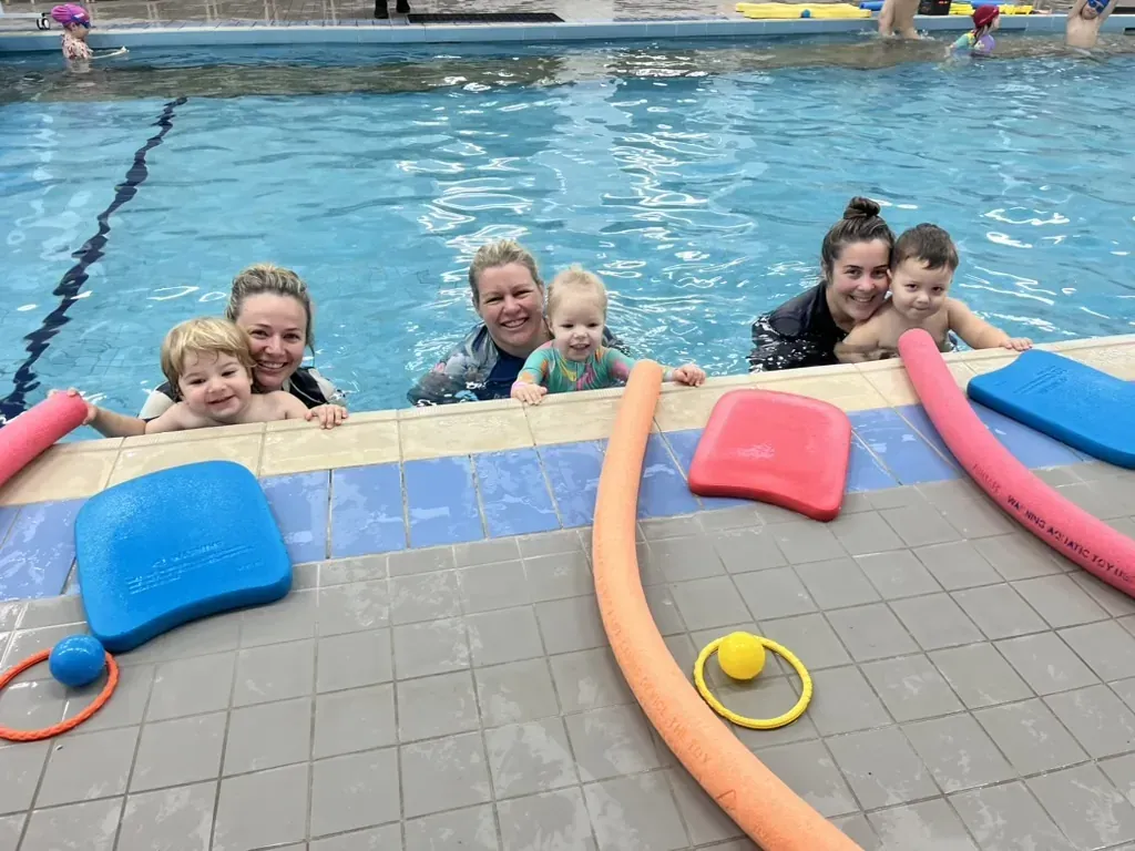 Mums and babies smiling at the camera beside the pool at Pod Squad