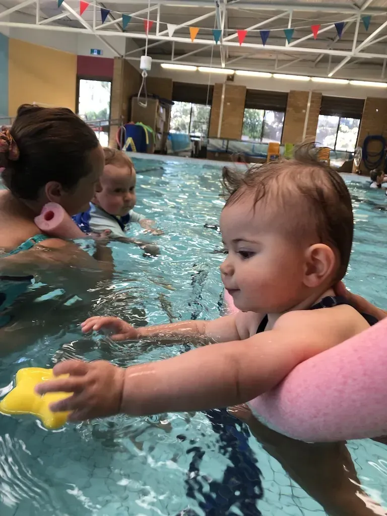 A baby reaching for a floating toy during a Pod Squad baby swimming lesson