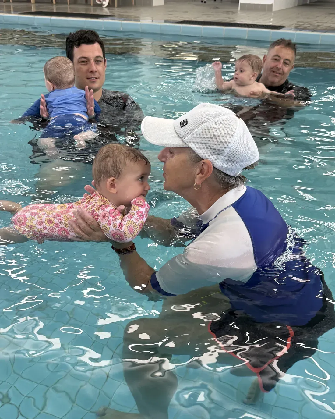 A Pod Squad instructor gently guiding a young baby nose-to-nose in the warm indoor pool