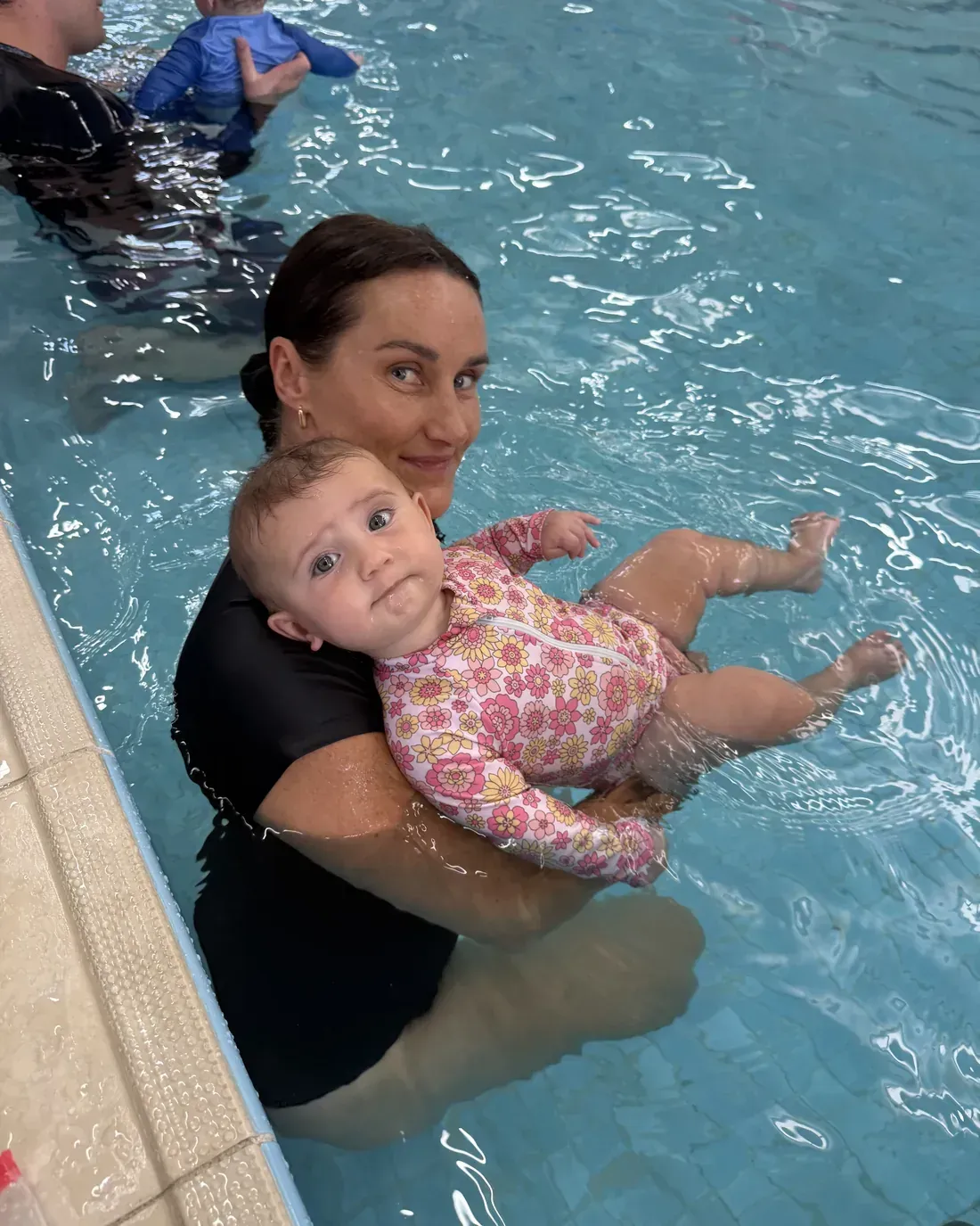 Jodie holding her baby Hazel, both smiling, during a Pod Squad baby swimming lesson