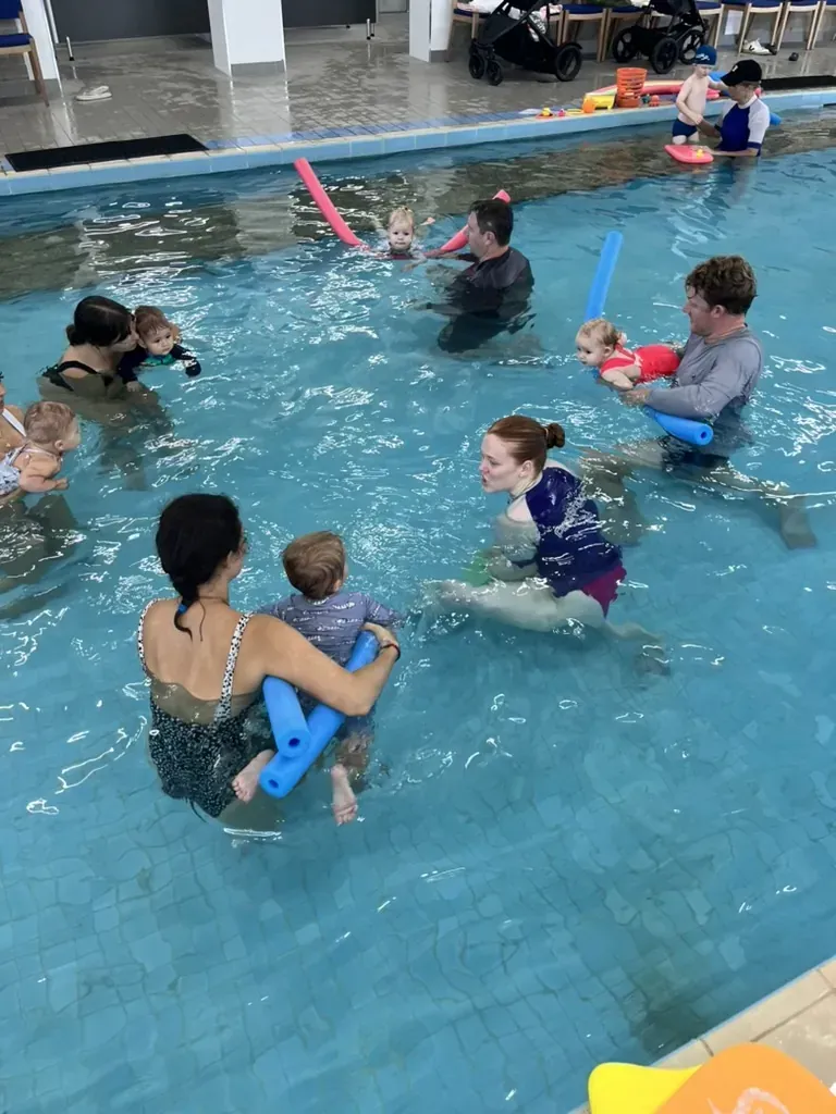 A Pod Squad baby swimming class with several parents and babies practising together in the warm pool