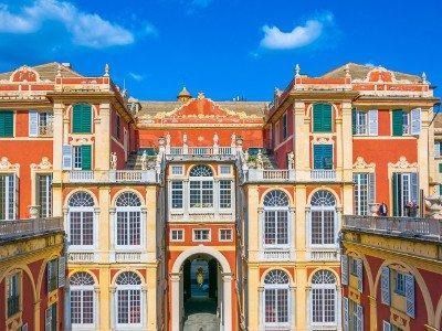 La facciata di un palazzo nei vivaci colori rosso e crema a Genova, presenta finestre simmetriche e un arco centrale.