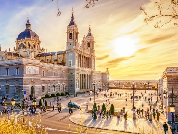 La Cattedrale dell'Almudena a Madrid al tramonto, con una grande piazza piena di gente in primo piano.