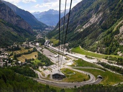 Vista dalla funivia , strade tortuose e l'ingresso del tunnel circondato da ripidi pendii montuosi.