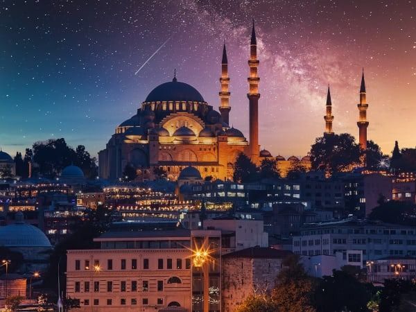 La Moschea di Solimano a Istanbul di notte, illuminata da un cielo stellato e colorato, con la Via Lattea visibile.