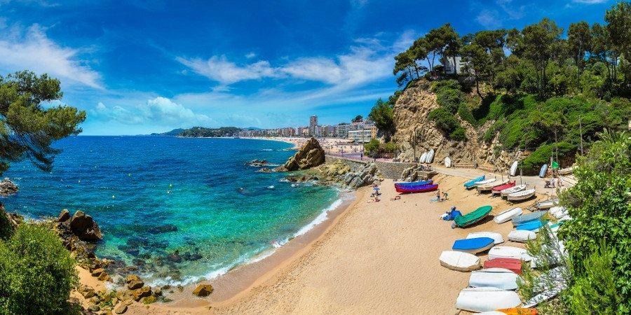 Una baia con acque turchesi, una spiaggia con piccole imbarcazioni e una scogliera rocciosa sotto un cielo azzurro.