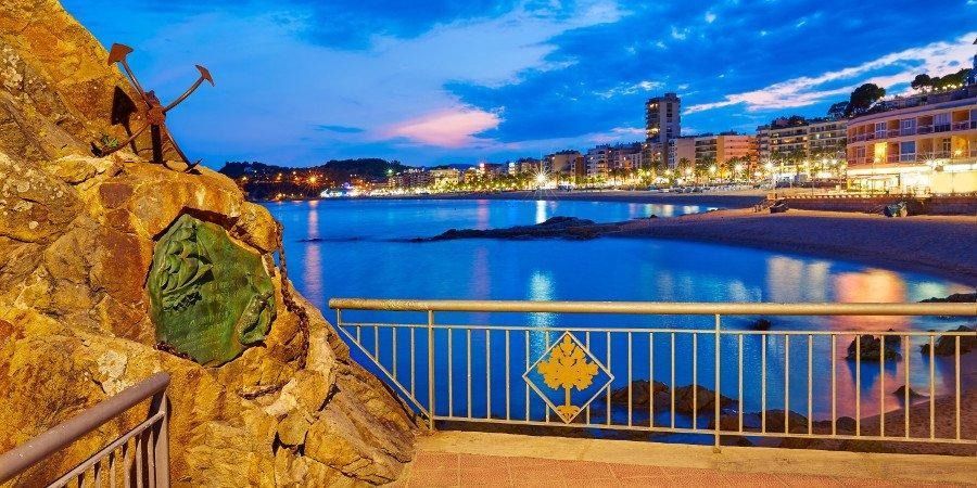 Una pittoresca cittadina, vista da un sentiero dotato di ringhiere metalliche che si affaccia su una tranquilla baia azzurra.