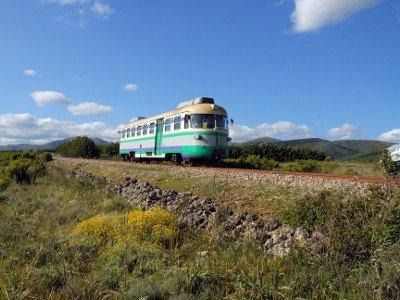 Un vagone ferroviario verde e bianco che viaggia sui binari in un paesaggio rurale e aperto, con montagne in lontananza.