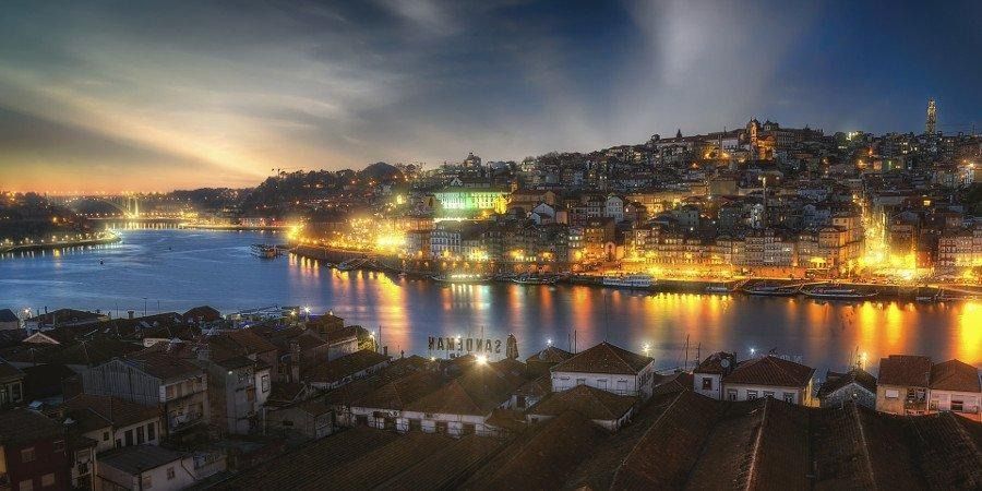 Una vista di Porto, all'ora d'oro, con gli edifici illuminati lungo il fiume Duero che si riflettono nell'acqua scura.