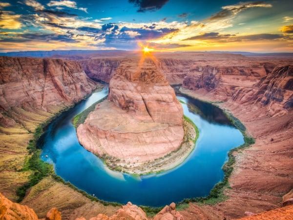 Un raggio di sole splende sopra l'Horseshoe Bend del fiume Colorado, un canyon circondato da ripida arenaria arancione.