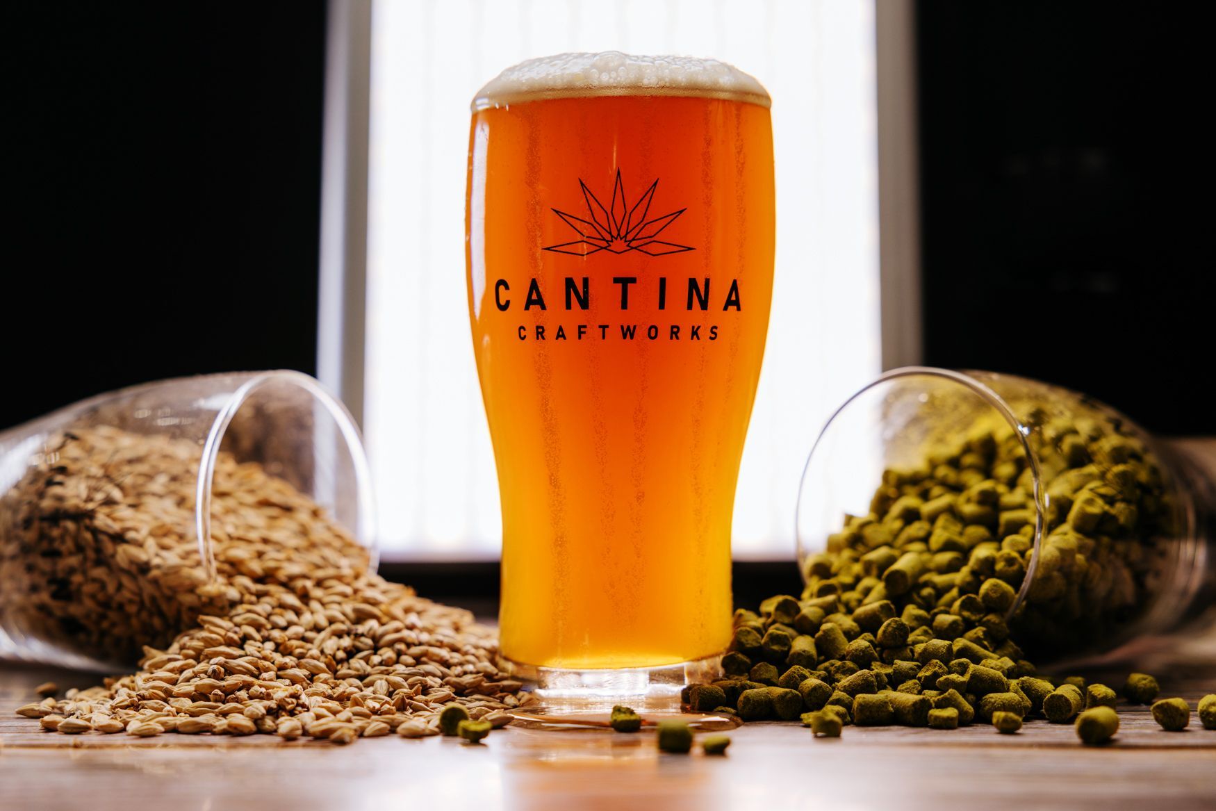 A glass of beer is sitting on a table next to grains and hops.