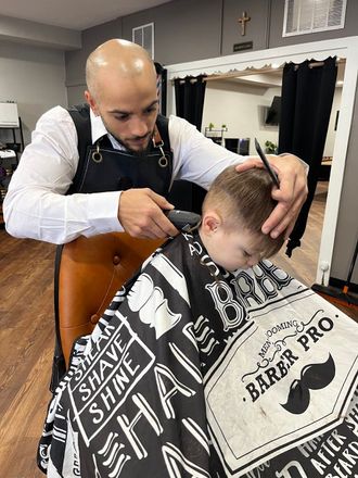 Barber cutting a child’s hair in a salon, using clippers and comb.
