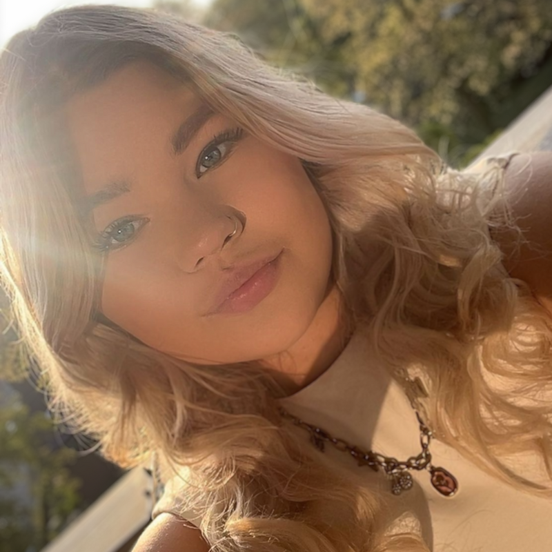 Blonde vrouw met blauwe ogen en een neusring lacht buiten in de zon.