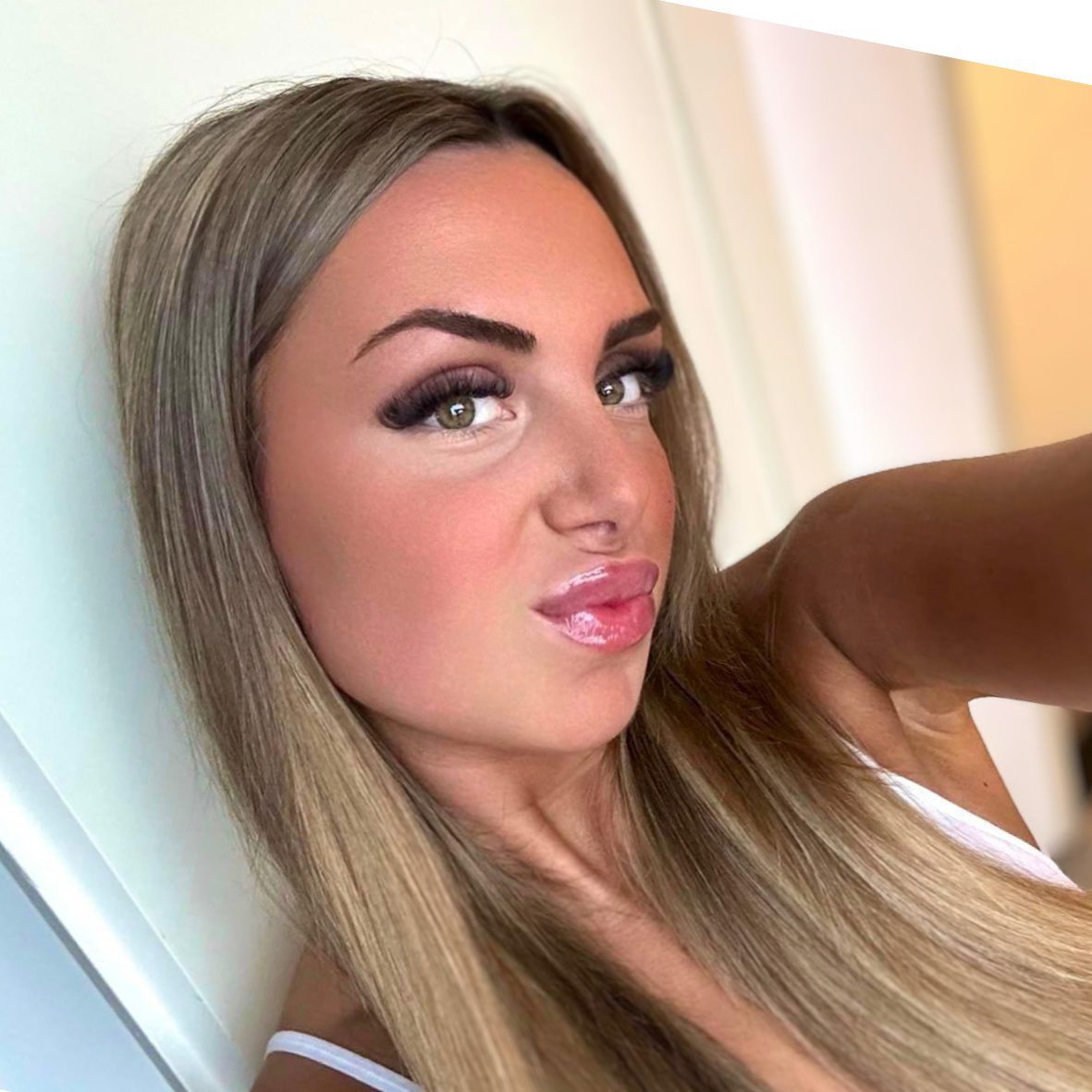 Een vrouw met lang blond haar, getuite lippen en een witte top kijkt in de camera.