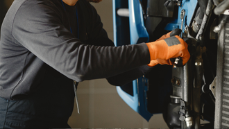 Mechanic in orange gloves working on a car engine with a wrench