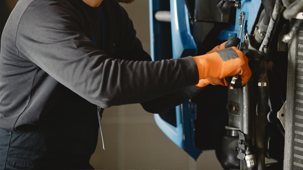 Mechanic in orange gloves working on a car engine with a wrench