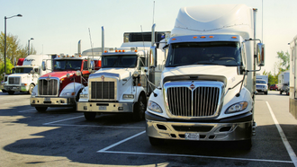 Three semi trucks parked in a lot, including red, beige, and white cabs under a bright sky