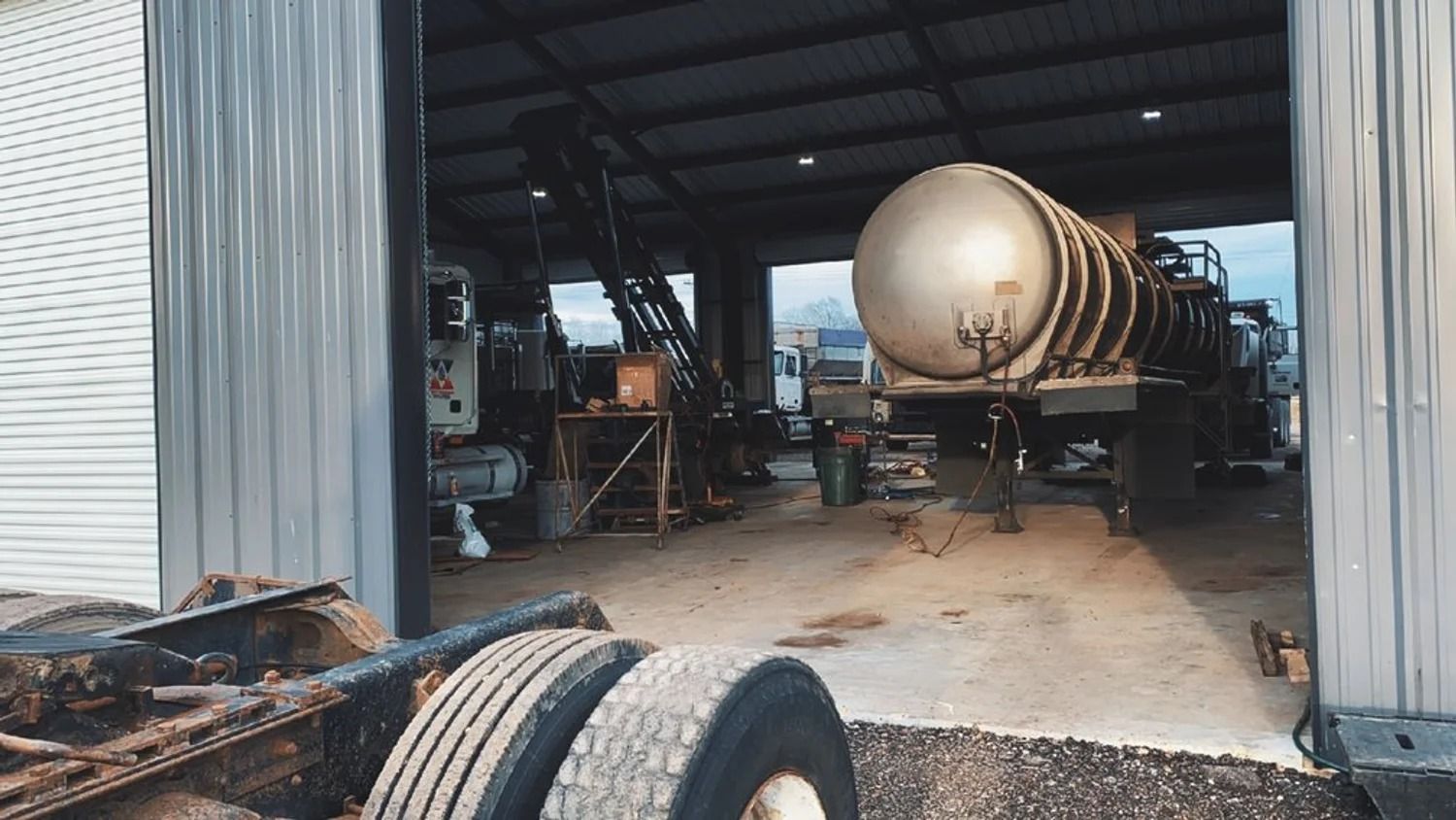 Large tanker trailer inside an industrial shed, with a tire and metal doorway in the foreground.