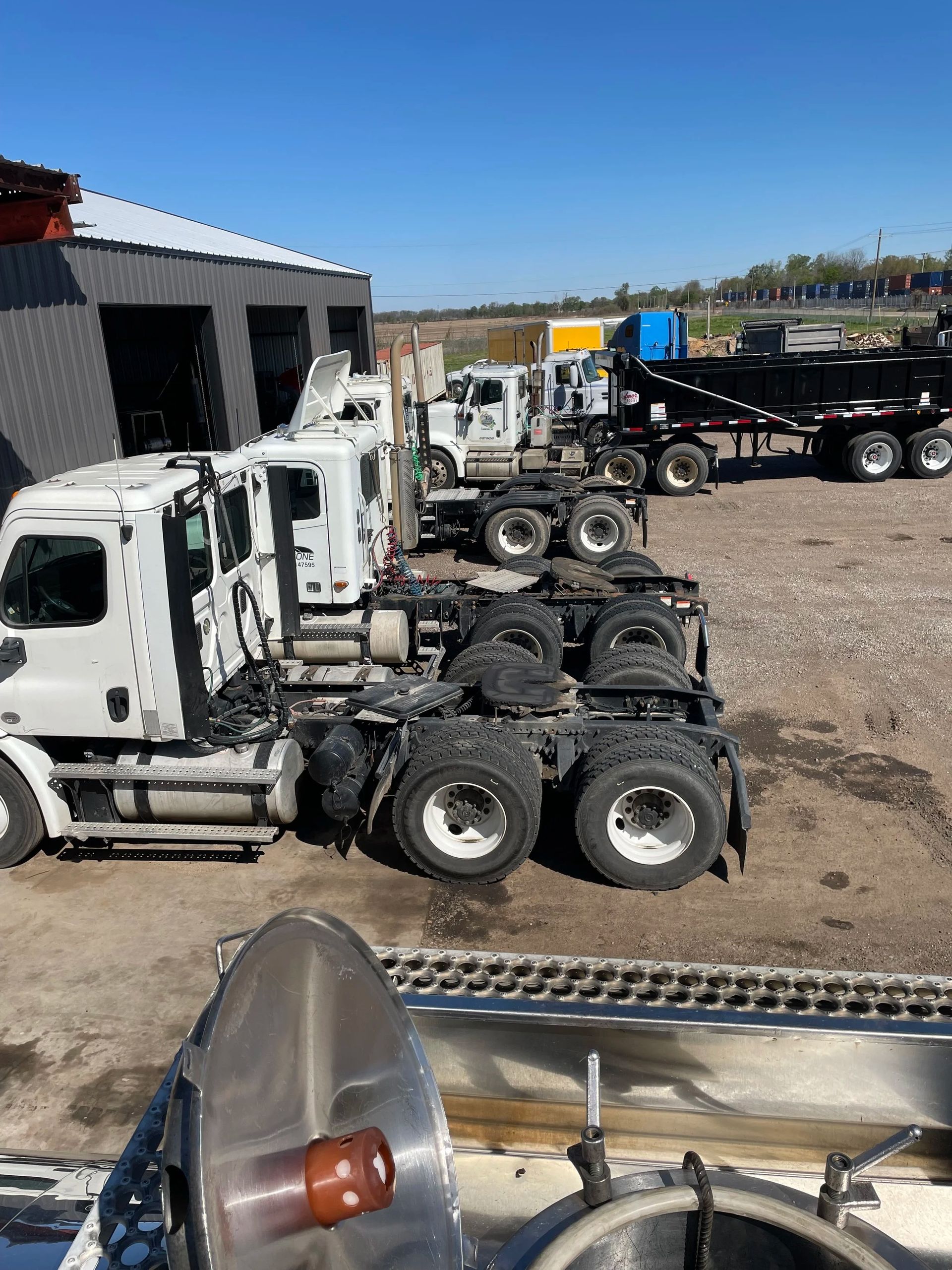 White semi-truck tractors parked in a gravel lot beside a warehouse under a clear blue sky