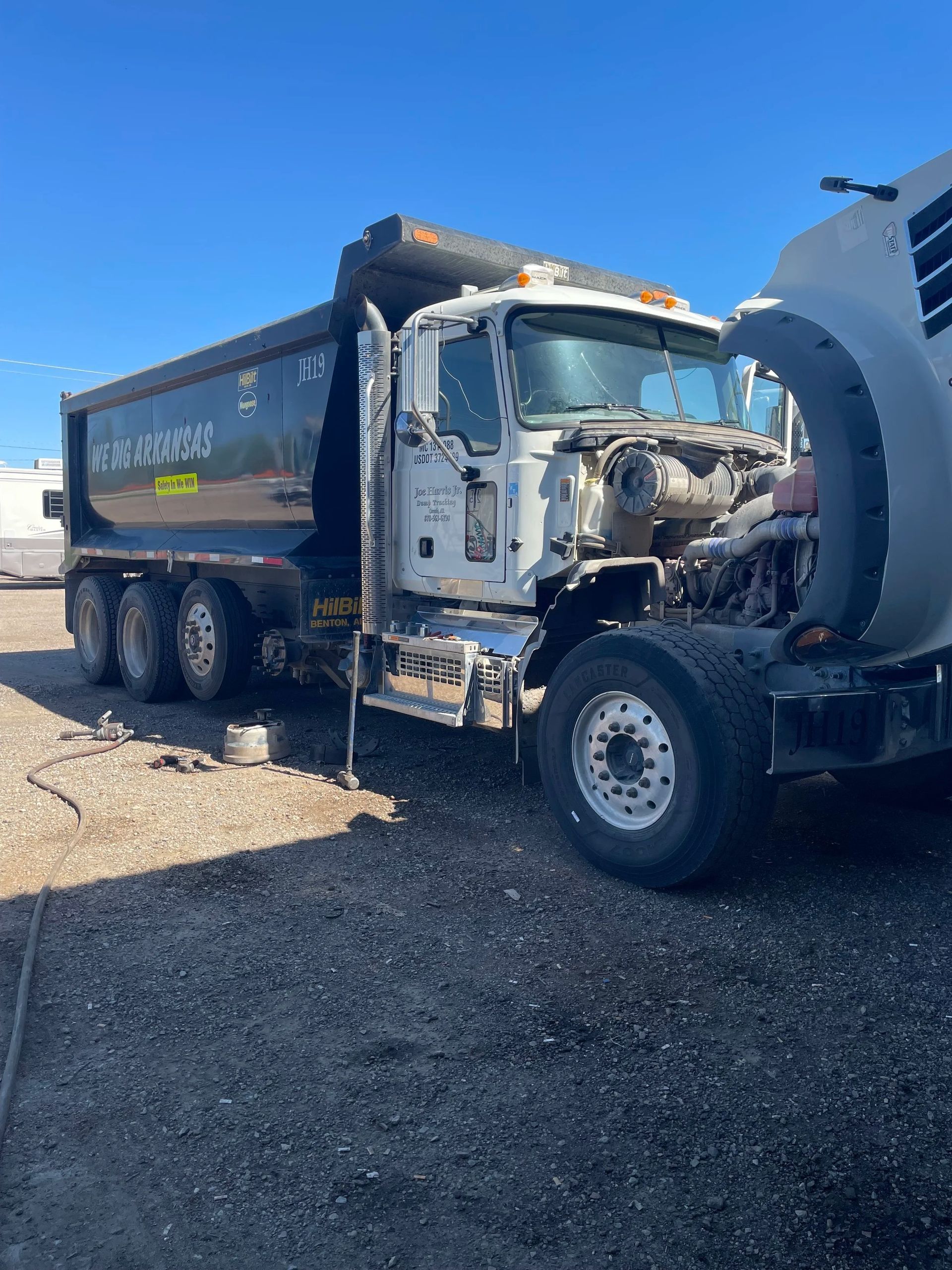 Damaged black dump truck with crushed front end parked on gravel lot under clear sky