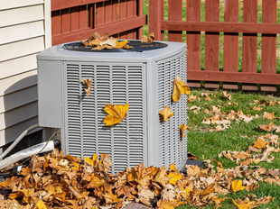 Central air conditioning unit outside a building, surrounded by leaves.