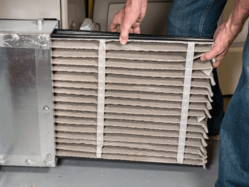 Person holding a dirty air filter, next to a furnace.